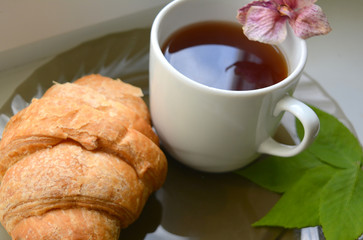 Beautiful composition: coffee, croissant, green leaves and dry orchid flower 