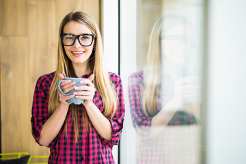 Young girl with cup of coffee with good mood in the morning in modern office near window