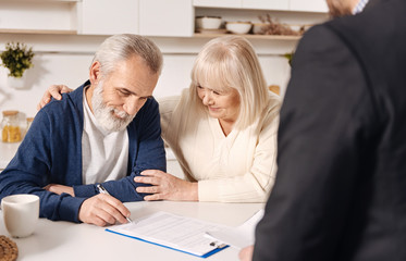 Charming cute elderly couple signing documents at home