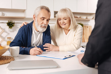 Delightful elderly couple signing documents at home