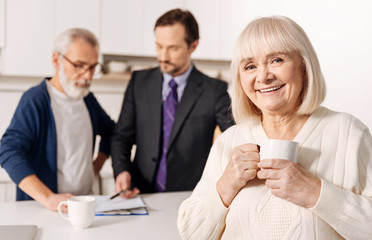 Glad elderly woman relaxing while her husband meeting with lawyer