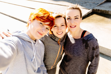 fitness, sport, people and lifestyle concept - smiling three woman doing selfie outdoors on city street