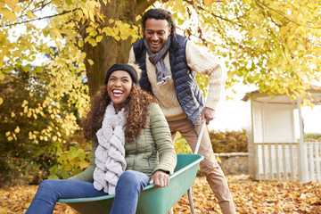 Naklejka premium Man In Autumn Garden Gives Woman Ride In Wheelbarrow