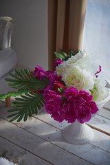 Vase and white and purple fluffy peonies placed on a wooden floor in a room