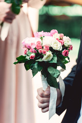 fiance in a dark blue suit holds a wedding bouquet made of roses