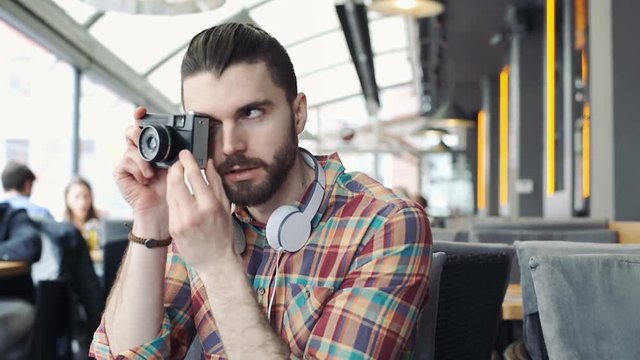 Handsome man looks happy while sitting in the cafe and doing photos on old camera
