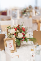 red and ivory floral arrangement prepared for reception, wedding table with candle and setting, winter concept