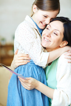 Mother with greeting-card embracing her daughter