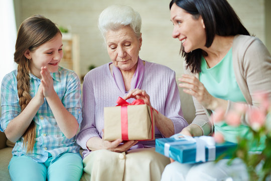Young woman and her daughter looking at senior female unpacking gift