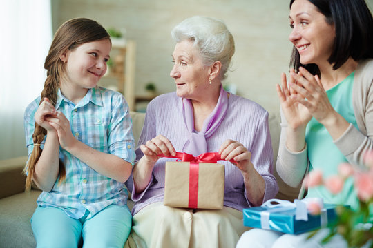 Aged woman with gift and her daughter and granddaughter applauding