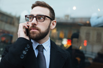 Elegant man in eyeglasses talking on cellphone outdoors
