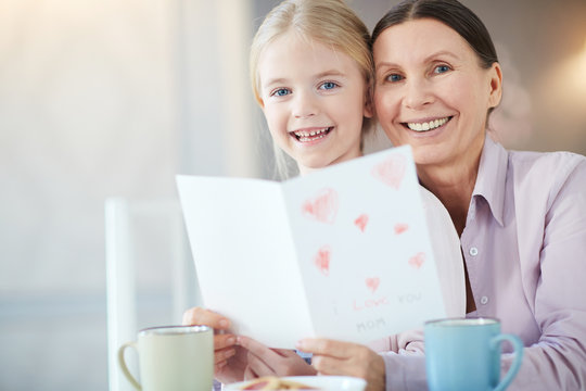 Senior woman and little girl with greeting card looking at camera
