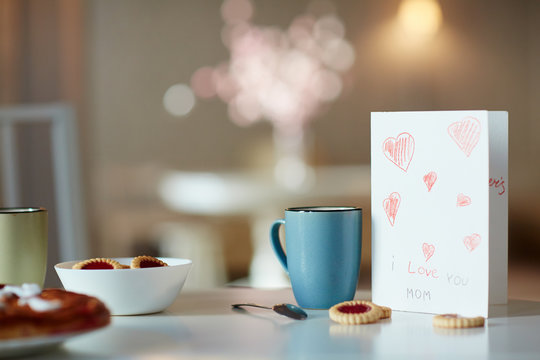 Paper greeting card for mother, mug with drink and biscuits on table