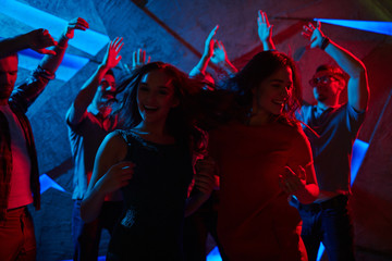 Obraz na płótnie Canvas Ecstatic girls dancing by disco music with guys on background