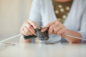 Closeup portrait of gentle hands of mature woman knitting scarf at table in home interior