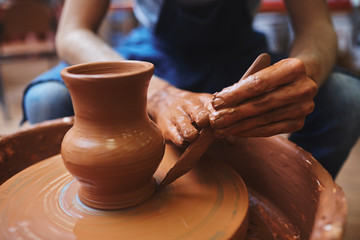 Potter using hand-tool for correcting edges of rotating jug