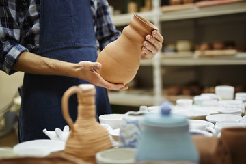 Young craftsman holding jug over collection of crockery