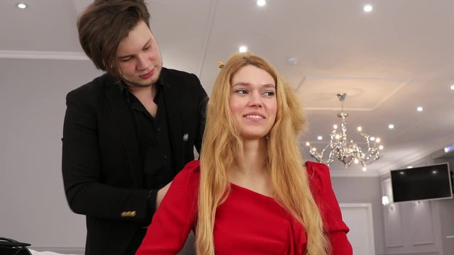 Young stylist men does hair styling to a beautiful girl in a beauty salon