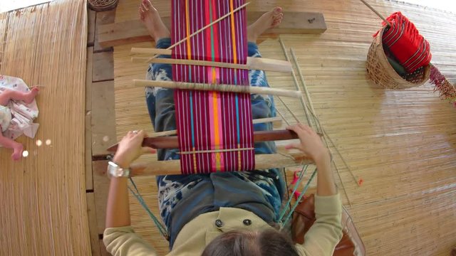 Woman weaves intricate patterns on loom as baby lies alongside