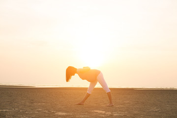 silhouette of pregnant mother performing yoga on beach during sunset
