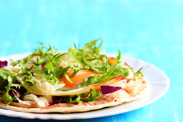 Homemade tortilla with fried egg, salad mix, hummus and parsley on a plate. Blue wooden background. Healthy and quick tortilla with filling. Closeup