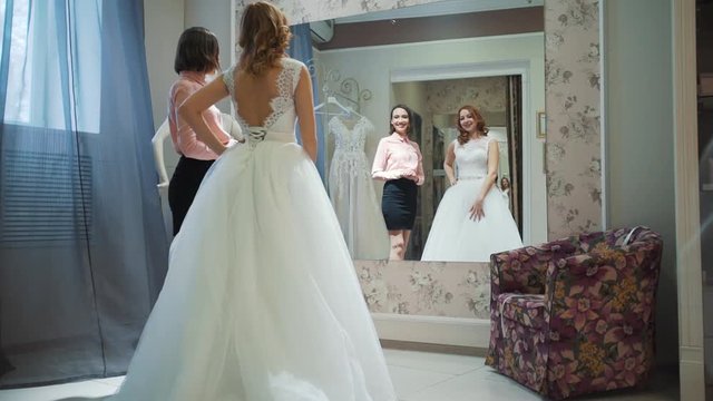 Female trying on wedding dress in a shop with women assistant.