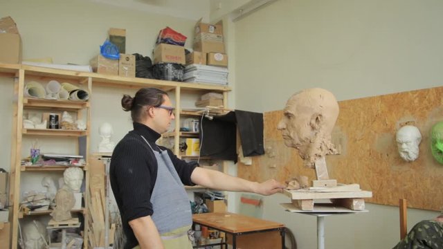 Sculptor modelling sculpture adjusting face details head made of clay. Creative concept.