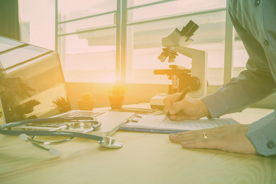 Doctor's hand working using pen writing on patient's discharge blank paper form, medical prescription, stethoscope on table/ desk: Physician taking note in hospital,clinic interior,vintage color - Powered by Adobe