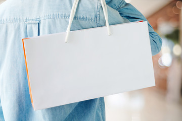 Hand holding white shopping bag on blur store background with copy space for text, template, business concept