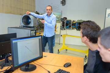 Obraz premium Students at computer looking at teacher with model
