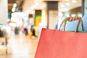 Hand holding red shopping bag on blur store background with copy space for text, template, business concept