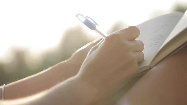 Woman sitting at balcony and writing in diary with garden on the background