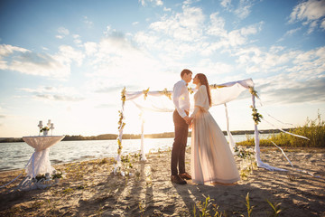 Couple in love holding hands near decorations and arch for wedding ceremony on beach. Honeymoon at...
