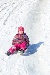 Fototapeta na wymiar Happy child sliding from a snowy hill. Active winter leisure outdoors