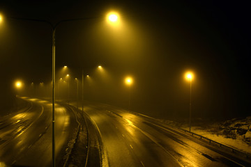 Foggy empty highway with street lights at night.