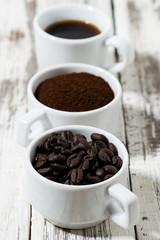 Three types of coffee - ground, grain and beverage in cups on white table, vertical