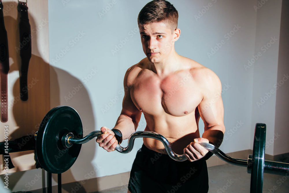 Wall mural muscular man working out in gym doing exercises with barbell, strong male naked torso abs