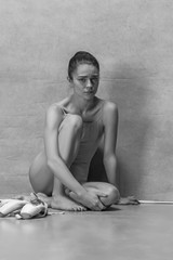 Tired ballet dancer sitting on the wooden floor on a pink background