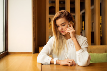 Fototapeta premium A girl is sitting in a cafe and using a smartphone, typing on the phone