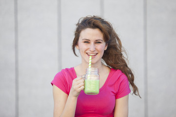 Young healthy teen girl drinking a green nutritional juice with a straw and smiling