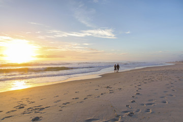 People walking on a beach into the distance, as the sunrises over the ocean