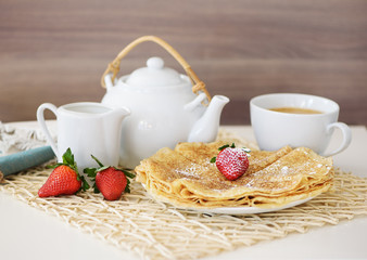 Pancakes with a strawberry and hot tea in the teapot and cup