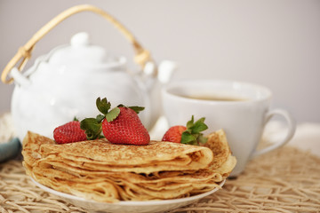 Pancakes with a strawberry and hot tea in the teapot and cup