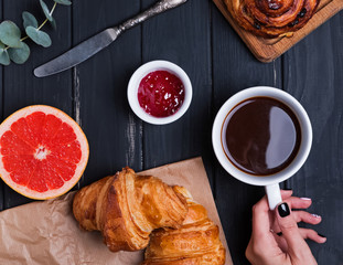 Delicious breakfast with croissants and woman's hand holding cupof coffee on the black table,