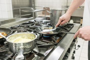 Koch oder Chefkoch im Restaurant brät Karpfen Fisch in Pfanne auf dem Herd