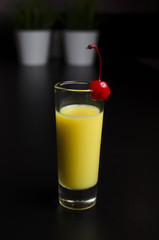 Yellow cocktail in a glass with cherry on a black background