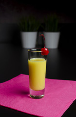 Yellow cocktail in a glass with cherry on a black background