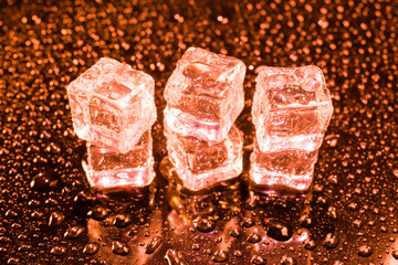 Ice cubes in red light on black wet table.
