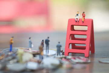 Miniature people: the recruiter sitting on top of red wooden ladder stack for finding the candidates on the coins stack, recruitment process, HR, HRM, HRD concepts.