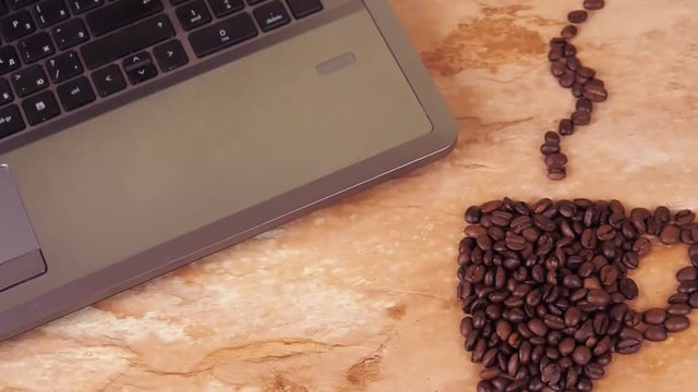 A cup of coffee beans with a laptop. On a kitchen marble table a sign of a cup of coffee beans and a laptop. Close-up.